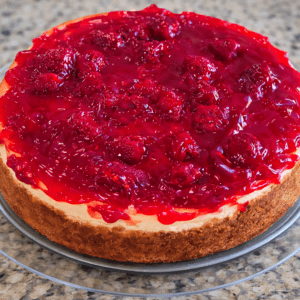 Cheesecake topped with raspberry glaze on plate.