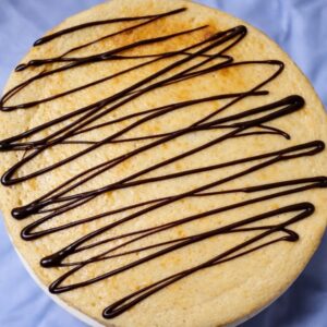 Cake topped with chocolate drizzle on blue.
