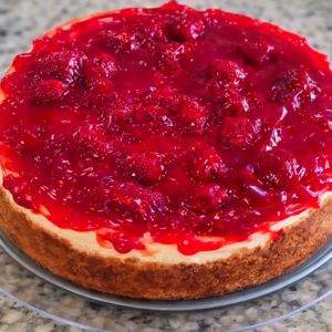 Cheesecake topped with raspberry sauce on plate.